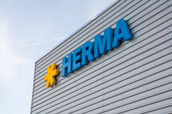 The company logo of HERMA in blue lettering with a yellow star on a gray wall.