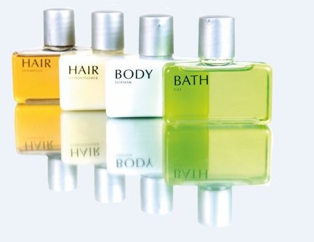 Four bottles of personal care products: shampoo, conditioner, body lotion, and shower gel, arranged on a reflective surface.