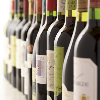 A row of wine bottles with various labels standing on a table. The bottles are arranged in different colours and shapes.