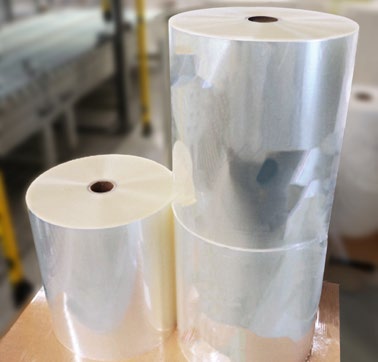 Transparent film rolls in various sizes, stacked on a table in an industrial setting.