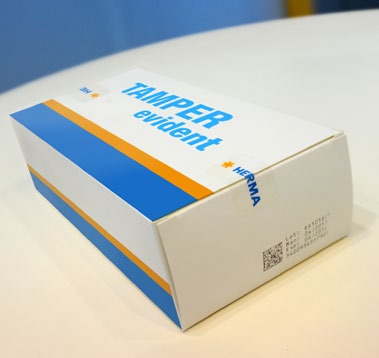 Packaging with the 'TAMPER evident' print in blue and orange, placed on a table.