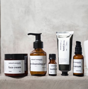 A range of natural cosmetic products, including face cream, cleansing gel, tooth oil, hand cream, and serum, set against a neutral background.