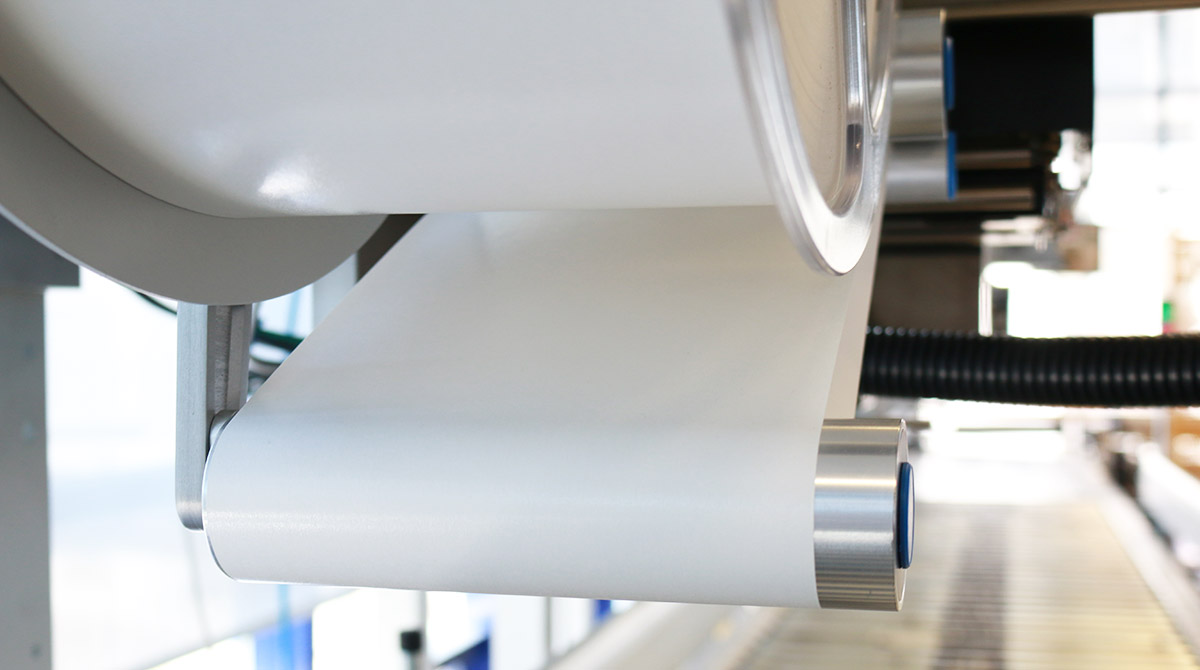 A roll of white paper being unwound by a machine, with a focus on the roller and the edge of the paper.