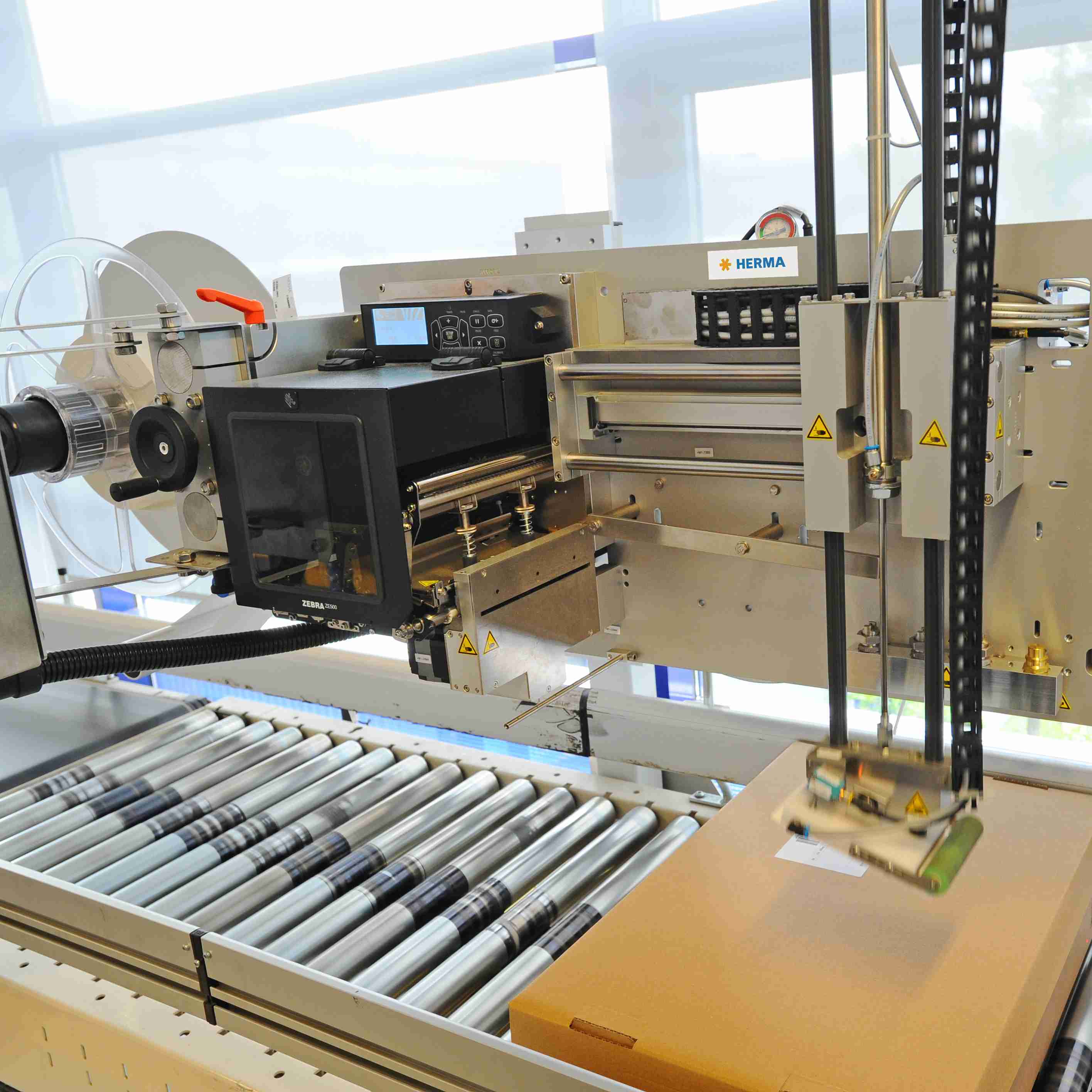 Automated labelling machine with a conveyor belt and control unit that labels boxes.
