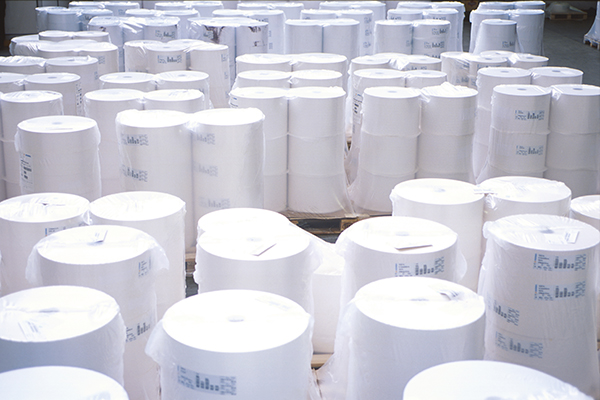 Rolls of paper, neatly stacked in a storage room, surrounded by more rolls of paper.