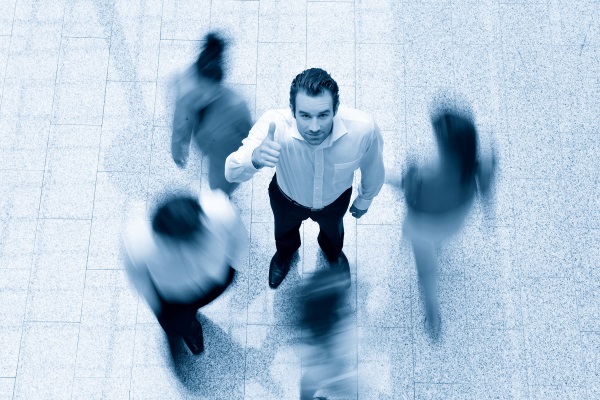 A man in a white shirt gives a thumbs up, surrounded by blurred figures in motion.