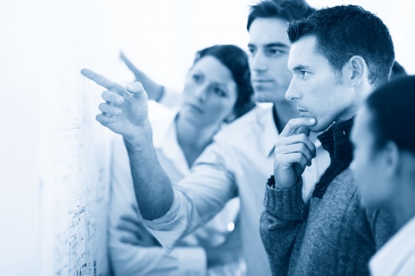 A group of four people is attentively examining a wall covered with diagrams and discussing it.