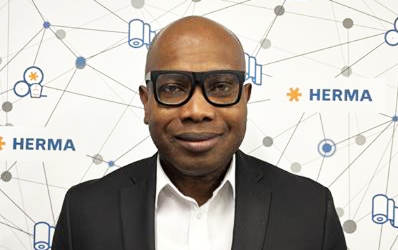 Man in glasses and a suit against a background with graphic elements and the HERMA logo.
